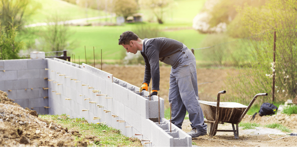 Man constructing a garden wall with concrete blocks.